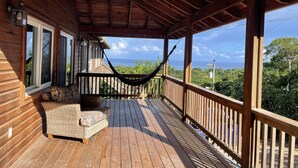 A wooden deck with a hammock, a wicker sofa, and a view of the ocean. - A Quiet East End Retreat. Ocean view with a private pool and custom water slide! (Bay Islands Department)