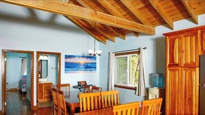 A dining area with wooden furniture, a painting of a sunset, and a window with curtains. - A Quiet East End Retreat. Ocean view with a private pool and custom water slide! (Bay Islands Department)