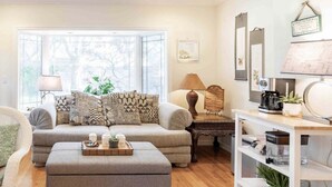 A cozy living room with a sofa, ottoman, and coffee table, a side table with a lamp, and a bookshelf with decorative items. - Bright Garden Guest Suite in Los Gatos, Heart of Silicon Valley (Los Gatos)