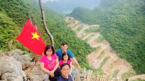 A group of people on a mountain trail with a flag, surrounded by lush greenery and winding paths.