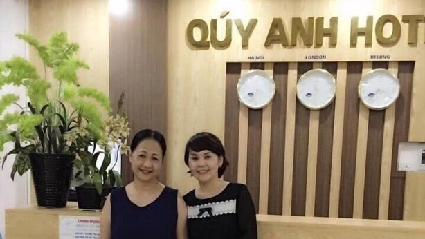A reception desk with a sign reading "QUY ANH HOTEL" and a wooden panel with three clocks.