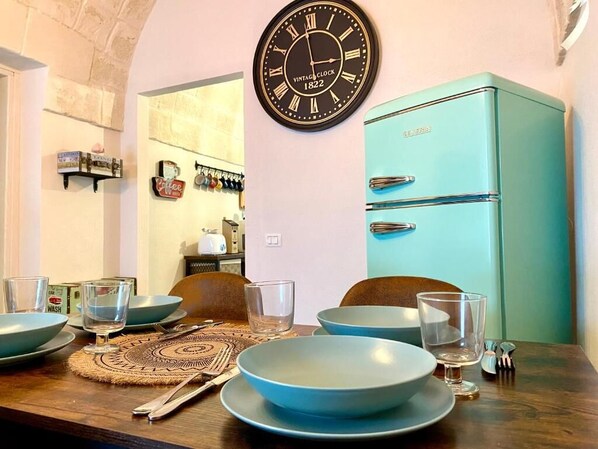 A dining table set with blue plates and glasses, a vintage clock, and a teal refrigerator.