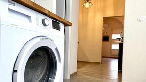 A front-loading washing machine in a modern kitchen with a wooden countertop and a hallway leading to another room. - The Pink Pumo (Monopoli)