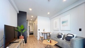 A modern living room with a flat-screen TV, a grey sofa, a wooden coffee table, and a dining area with a table and chairs.