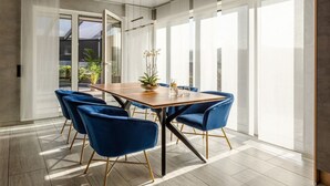 A modern dining area with a wooden table, blue chairs, and a large window providing natural light. - Modern Oasis w/ HotTub, View, Gym (Oberbettingen)