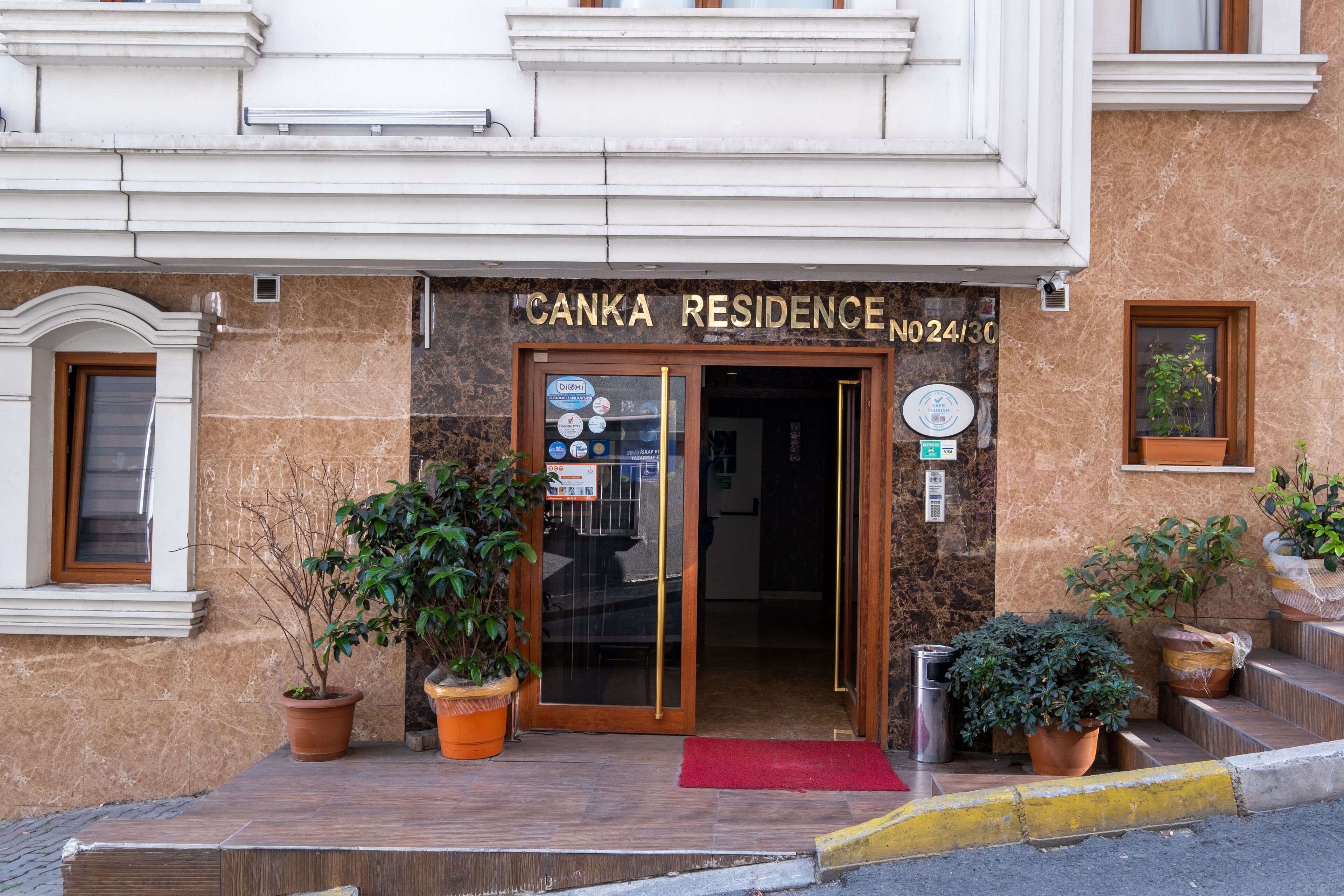 Exterior do Canka Residence, com fachada de mármore, porta de entrada em madeira e plantas em vasos.