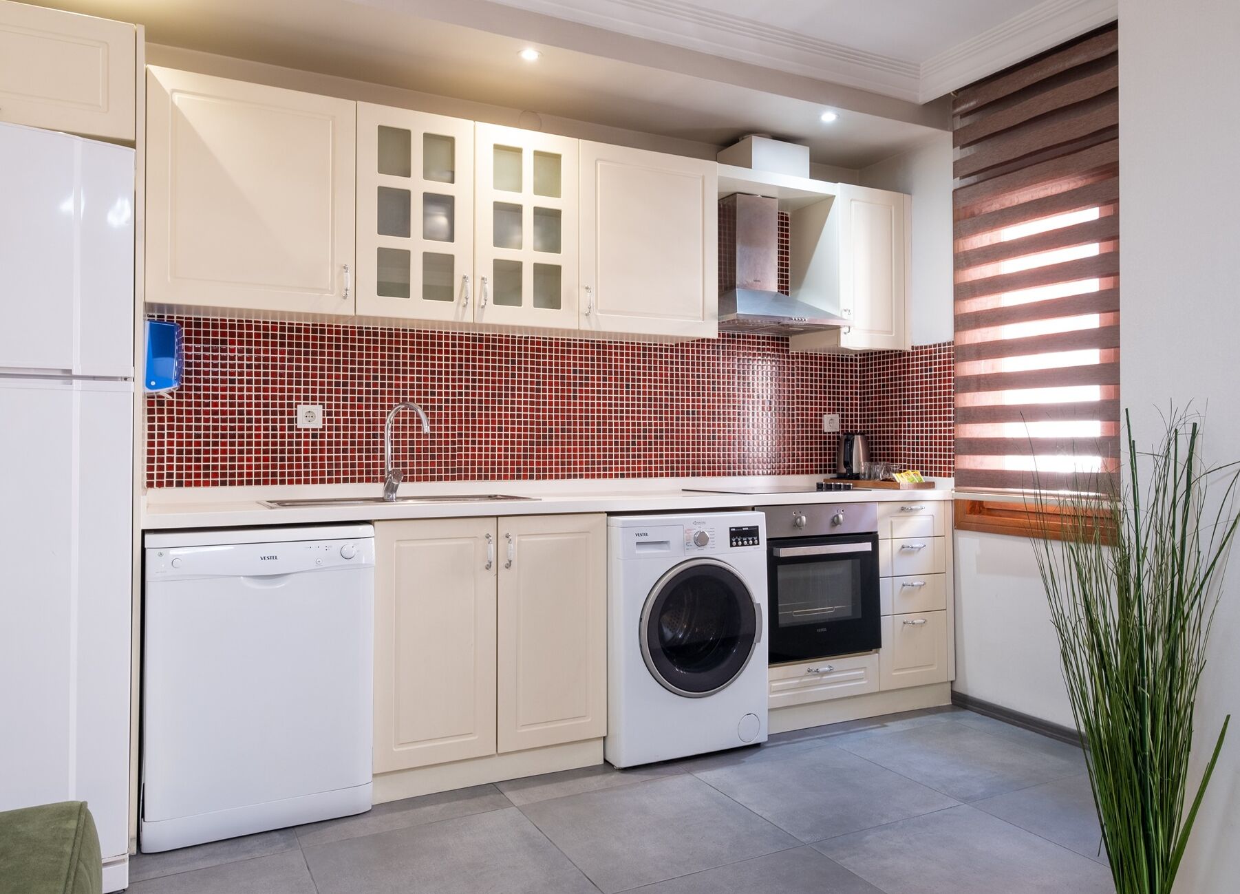 A modern kitchen with white cabinetry, a washing machine, an oven, and a tiled backsplash.