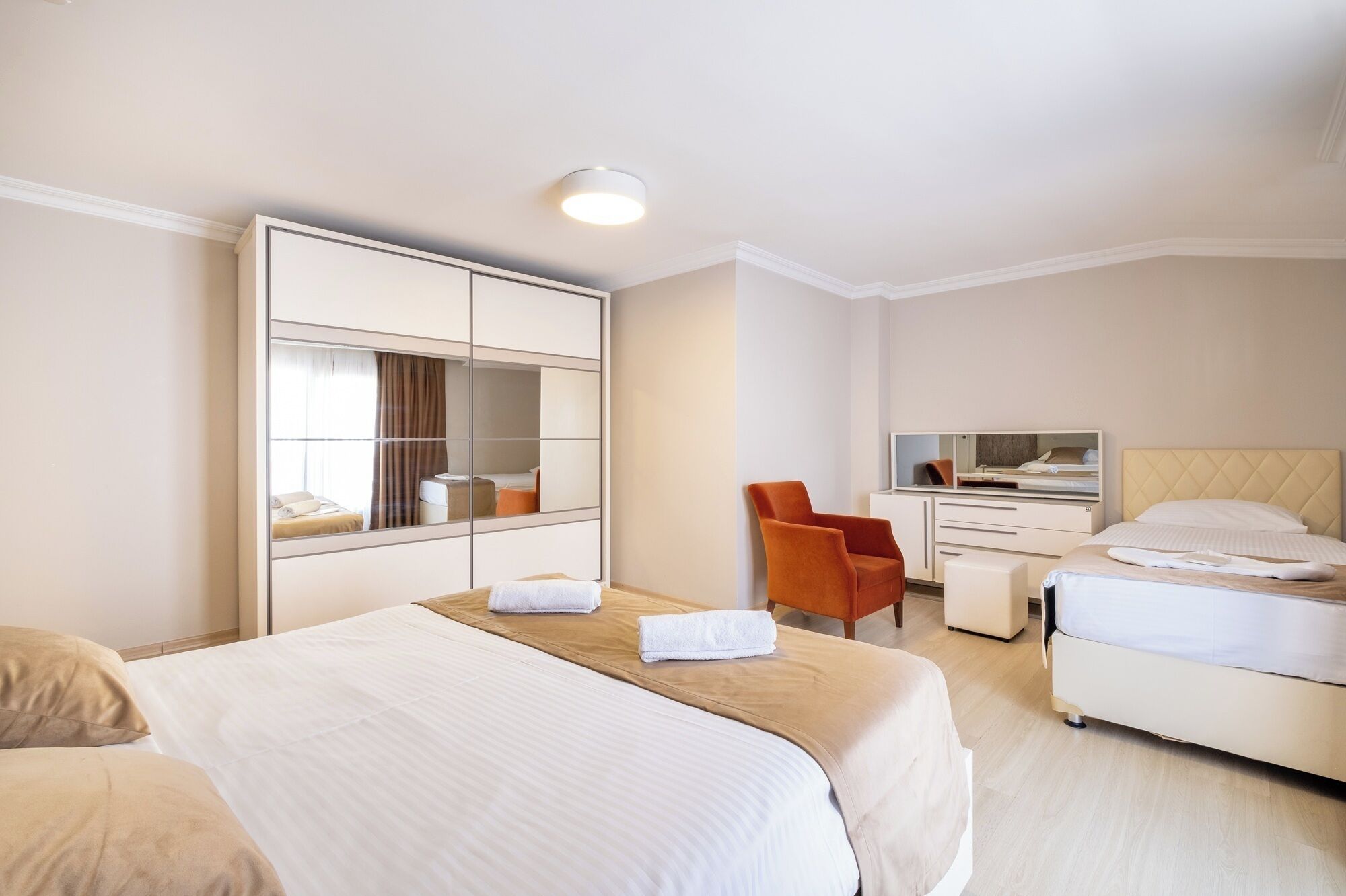 A hotel room with two beds, a desk, a chair, and a large mirror.