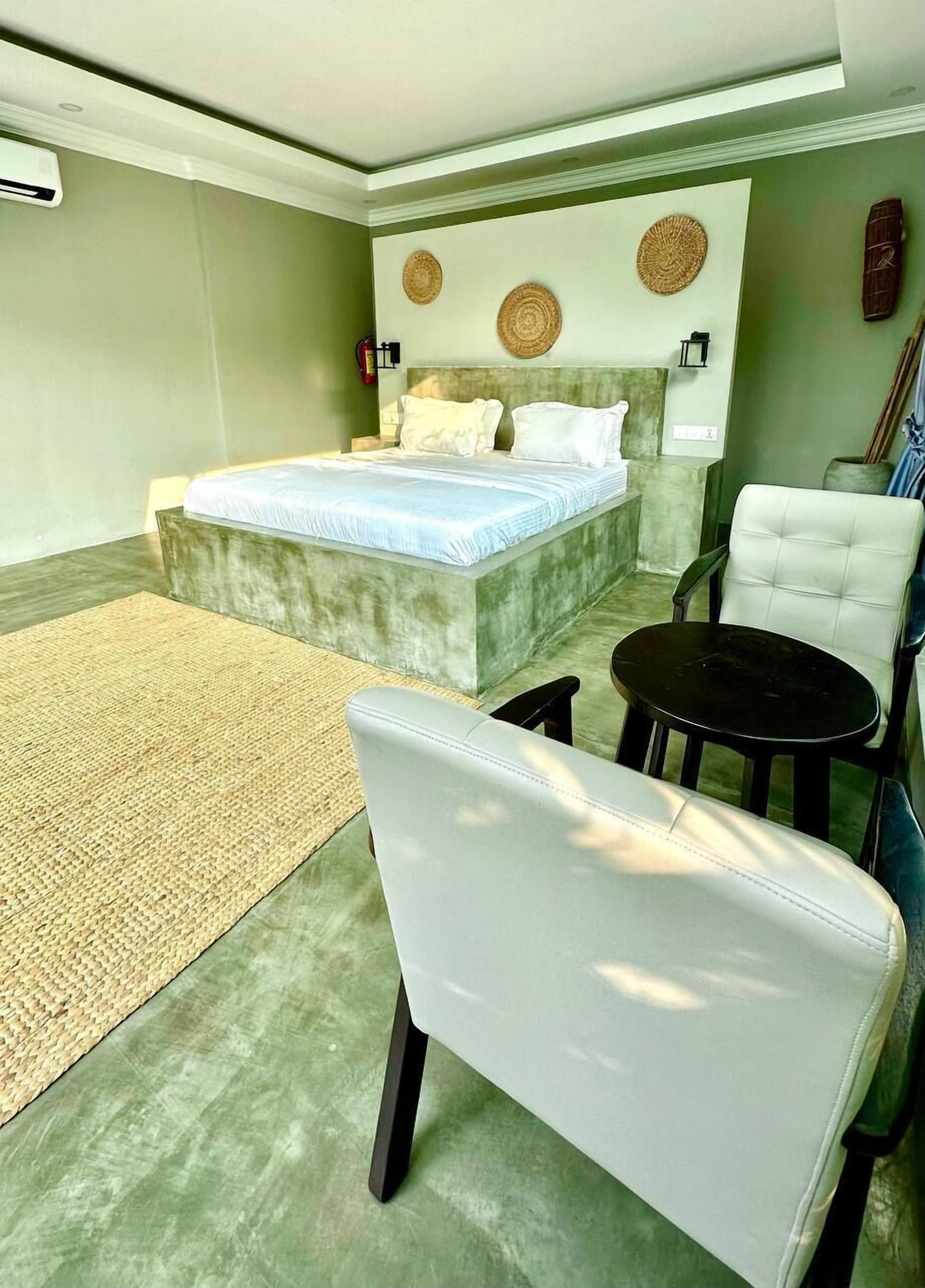 Een slaapkamer met een bed, een stoel, een tafeltje en een wandlamp.