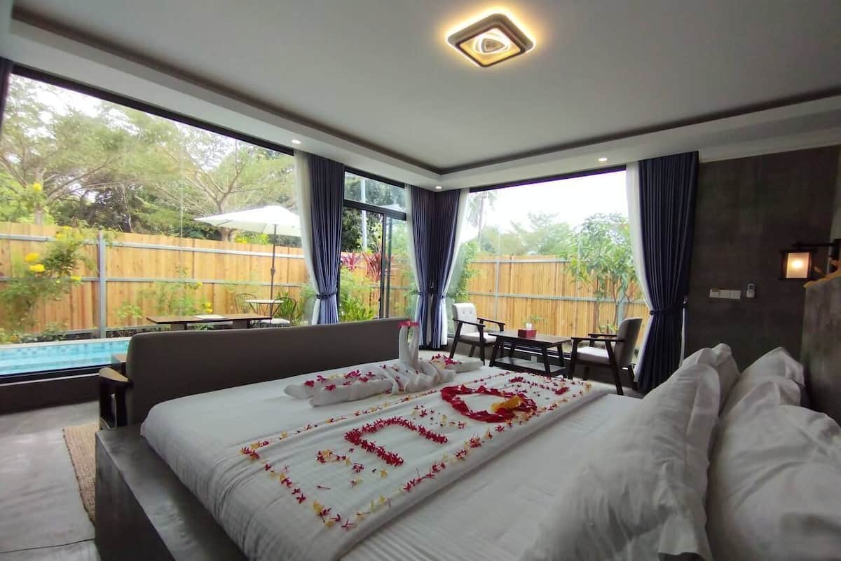 A bedroom with a large bed, a view of a swimming pool, and a dining area.
