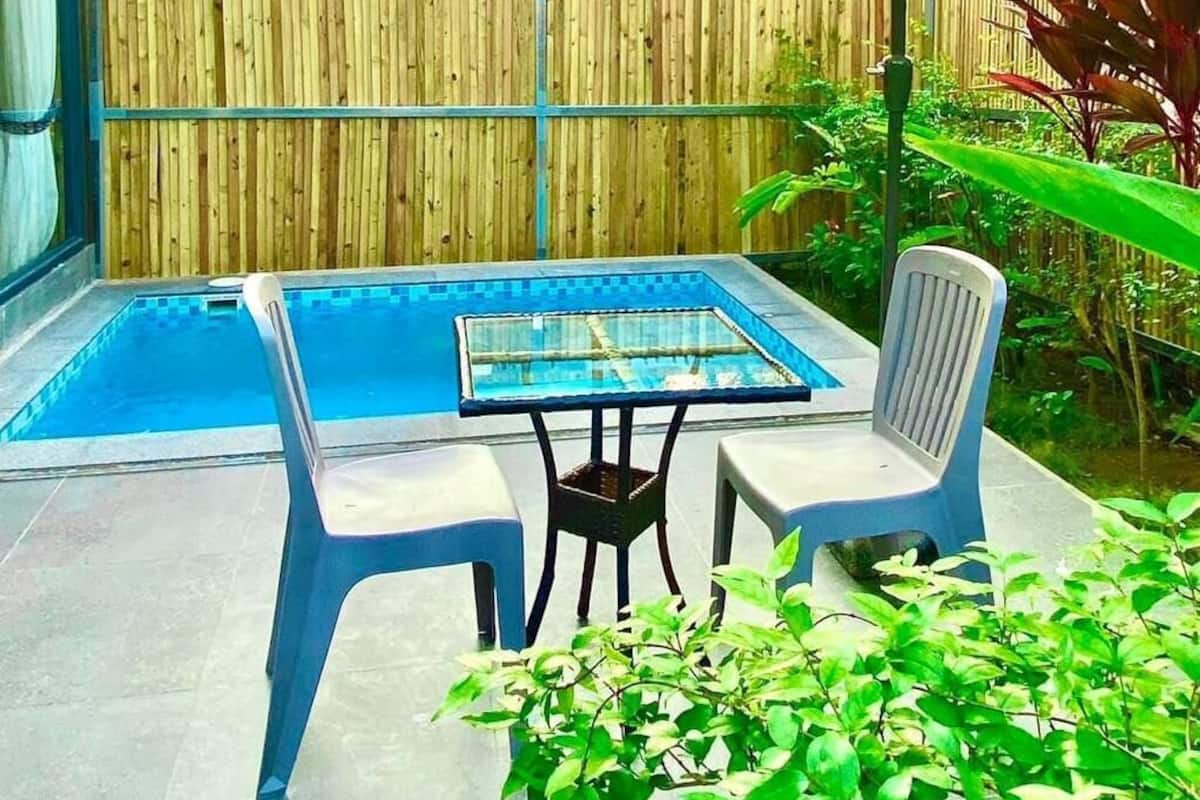 An outdoor pool area with a table and chairs, surrounded by a wooden fence and greenery.