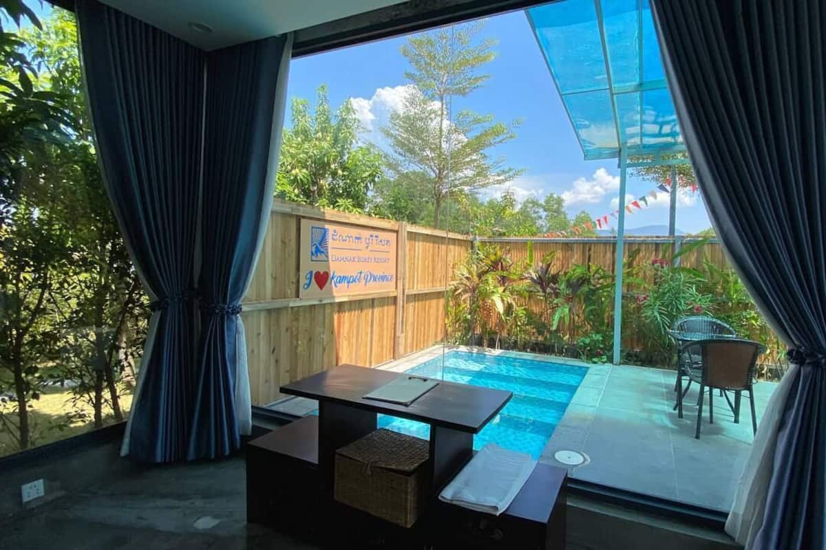 A room with a glass-enclosed pool, wooden deck, and a view of the surrounding greenery.