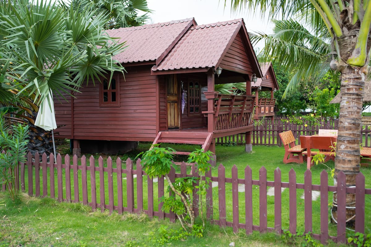 A wooden house with a porch, surrounded by a wooden fence and palm trees.
