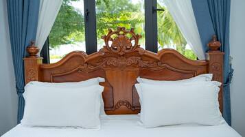 A wooden bed with white pillows and curtains, a window with a view of greenery.