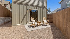 En uteplats med Adirondack-stolar och ett litet bord, omgiven av ett trästaket och ett grusunderlag.