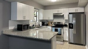 Una cocina moderna con armarios blancos, un refrigerador de acero inoxidable, un microondas y un horno empotrado.
