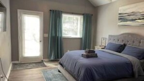 Un dormitorio con cama, ventana con cortinas, puerta y un cuadro en la pared.