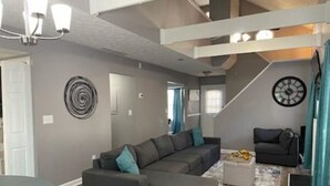 Una sala moderna con un sofá modular, una mesa de centro redonda y una escalera que sube a otro nivel.