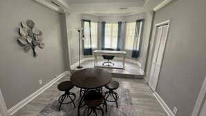 A dining area with a round table and four chairs, a decorative wall piece, and a view of a dining table through a bay window. - Roomy & Newly Renovated Guest House, Kitchen, Desk, Pet Friendly, Shared Patio! (Ellenwood)