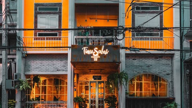 Un hotel con una fachada naranja brillante, un letrero que dice "TimeSabai" y un balcón con barandillas.