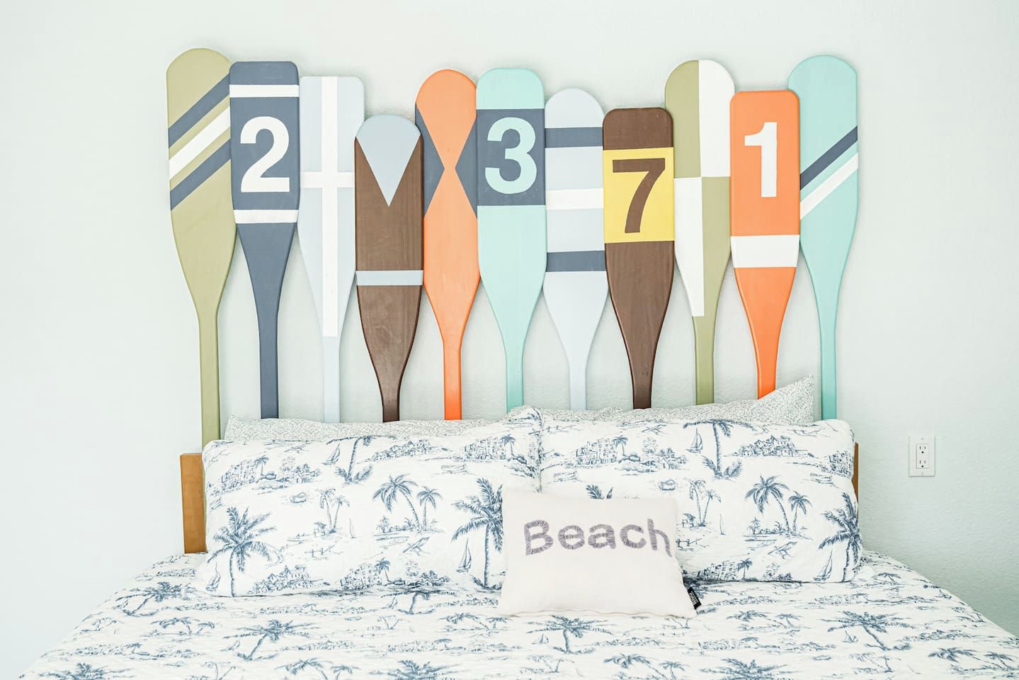 Una cama con una colcha de motivos playeros y una almohada que dice "Beach".