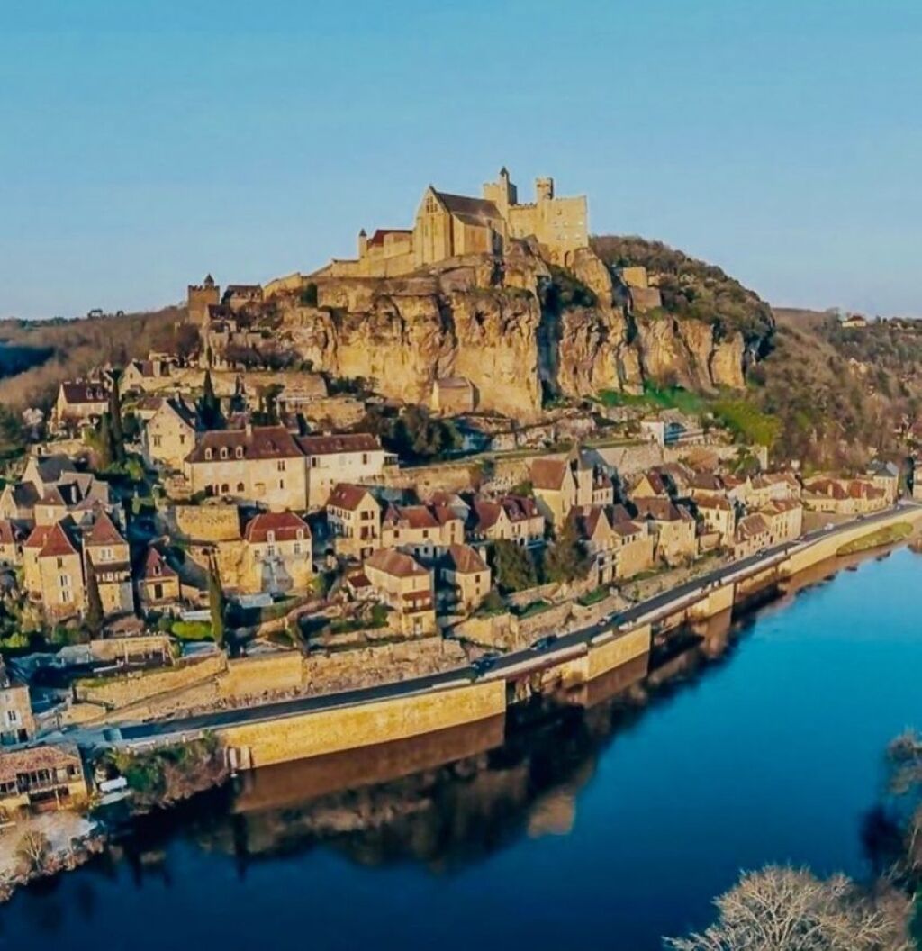 Una città storica con un castello imponente su una collina, collegata da un ponte a un fiume.