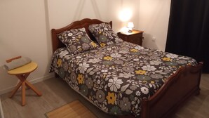 Ett sovrum med en säng i trä, sängkläder med blommönster, ett nattduksbord med en lampa och en stol.