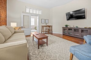 A living room with a sofa, coffee table, and TV. There is a dining area with a table and chairs. - Relaxing South Main Apartment with Modern Comforts (Saint Charles)