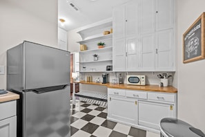 A compact kitchen with white cabinets, a stainless steel refrigerator, a microwave, and a checkered floor. - Relaxing South Main Apartment with Modern Comforts (Saint Charles)