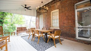 A covered outdoor patio with a brick wall, a wooden table with chairs, and a patterned rug. - 30-Night Minimum South Main Apartment (Saint Charles)
