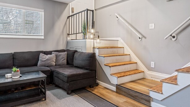 Ein modernes Wohnzimmer mit einem dunkelgrauen Ecksofa, einem Glastisch und einer Treppe mit Holzboden, die zu einer oberen Ebene führt.