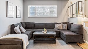 Ein modernes Wohnzimmer mit einem Ecksofa, einem Couchtisch und einem Fenster mit Jalousien.