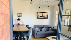 Un salon moderne avec un canapé gris, des coussins à motifs noir et blanc, une table basse en bois et un coin repas comprenant une table en bois et des tabourets de bar.