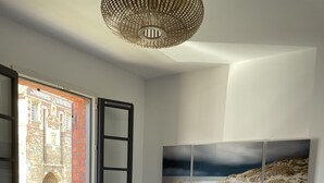 Une chambre à coucher avec un grand lit, une commode, un radiateur et une fenêtre donnant sur un immeuble et une voiture.