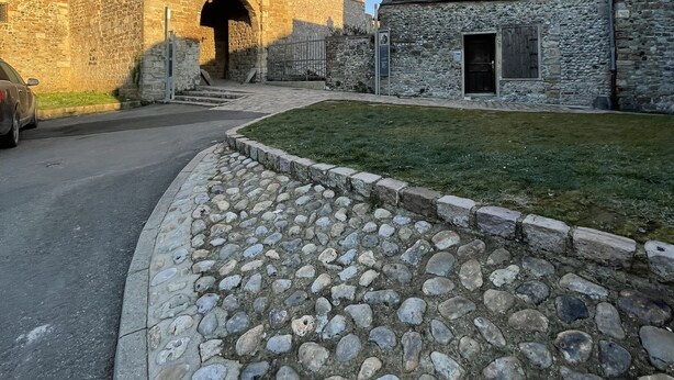 Un bâtiment en pierre doté d’une grande entrée en arc de cercle, d’une cour pavée et d’un bâtiment plus petit avec un toit en pente.