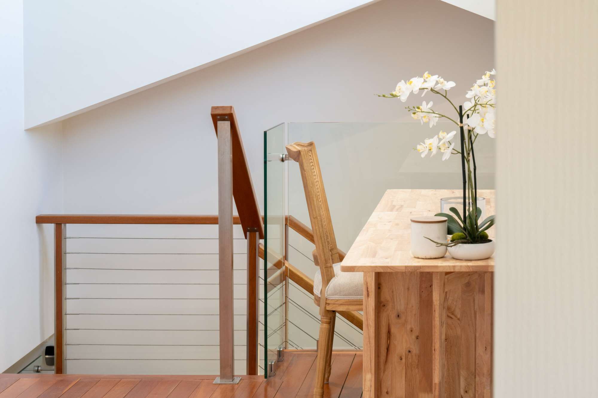 A wooden chair with a cushioned seat and backrest, a wooden table with a white vase and a potted plant, and a glass railing.