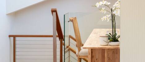 A wooden chair with a cushioned seat and backrest, a wooden table with a white vase and a potted plant, and a glass railing.