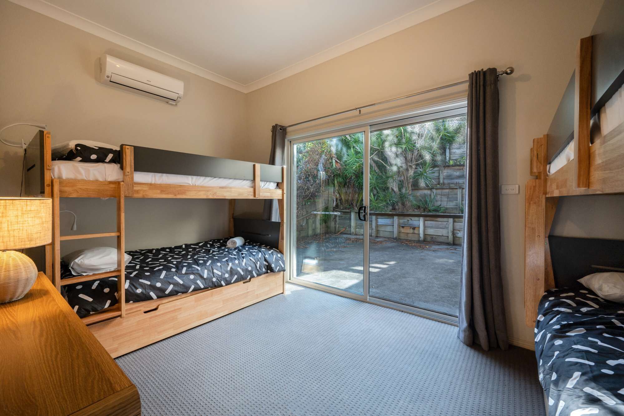 A compact room with bunk beds, a sliding glass door to a patio, and a small table with a lamp.