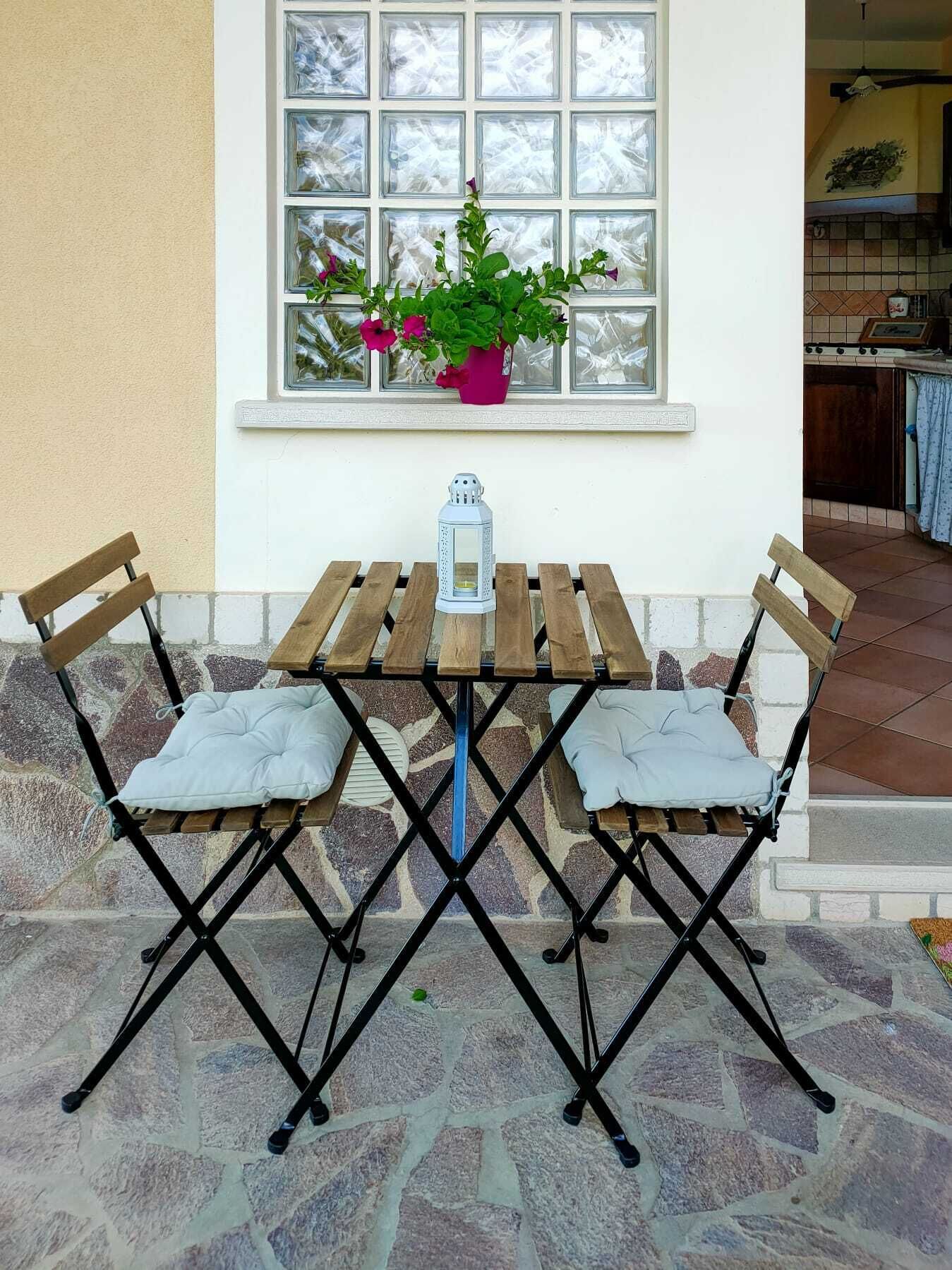 Una mesa de madera con dos sillas, un farol y una planta en maceta sobre el alféizar de una ventana.