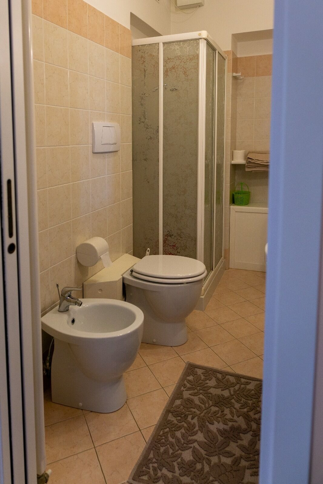 Ein Badezimmer mit zwei Toiletten, einem Bidet, einer Duschkabine und einem Handtuchhalter.