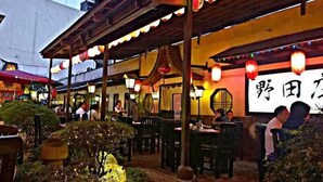 An outdoor dining area with tables and chairs, a covered seating area, and a large illuminated sign with foreign characters. - Dimacs Staycation  (Makati)