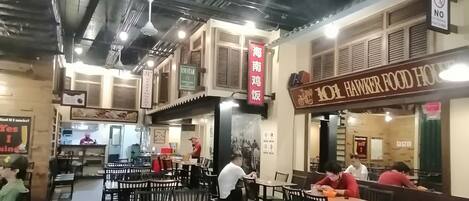 Interior de un restaurante con mesas y sillas, un letrero que dice '101 HAWKER FOOD HOUSE' y un cartel de 'NO LITTERING'.