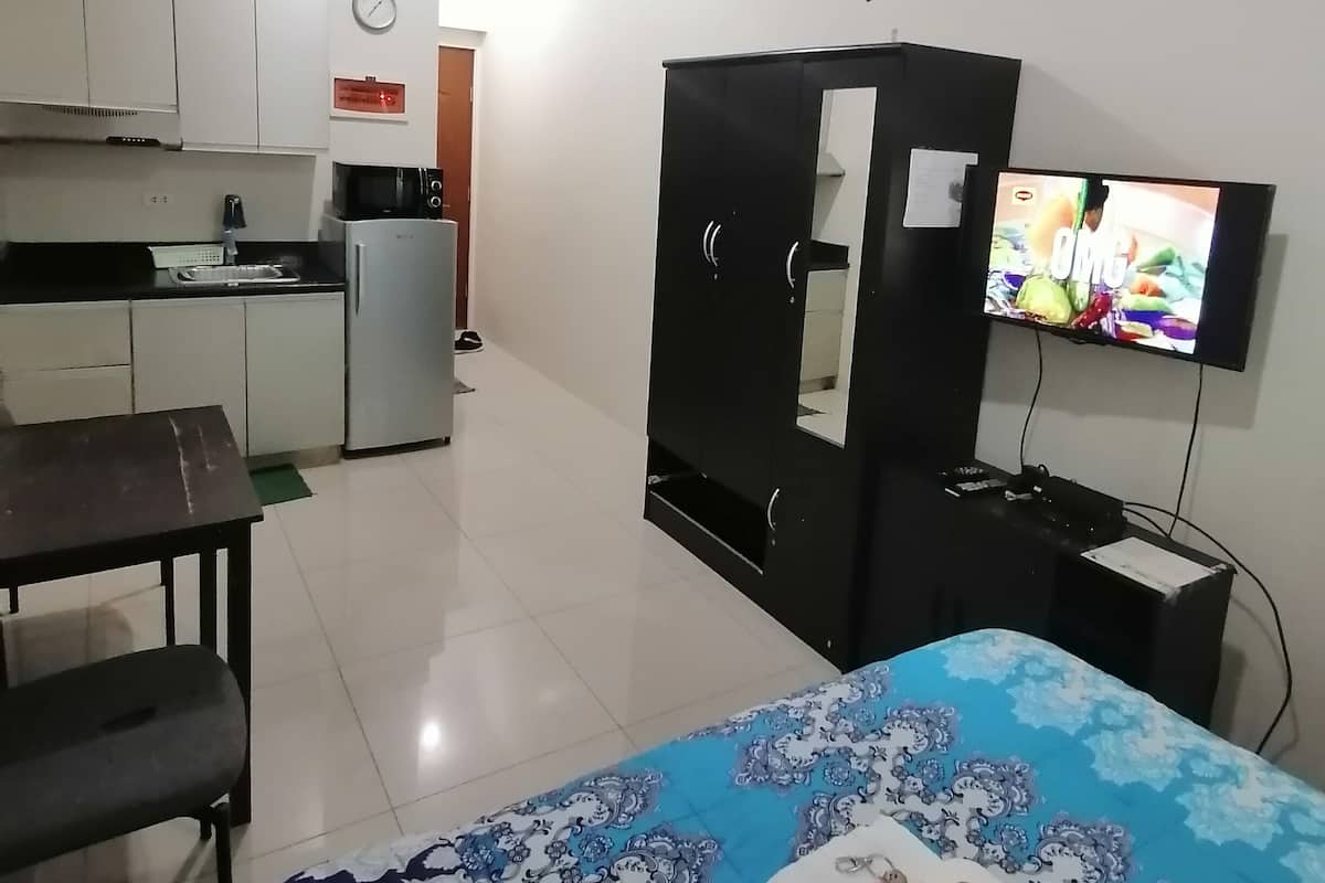 A compact living space with a kitchenette, a bed with a patterned bedspread, a television, and a ceiling fan.