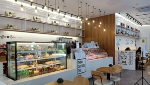A modern coffee shop interior with a bakery display, seating area, and a menu board. - Dimacs Staycation  (Makati)