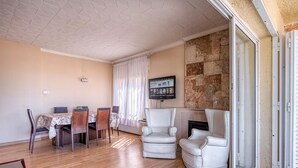 Uma sala de estar com lareira, uma área de jantar com mesa e cadeiras, e uma televisão fixada na parede.