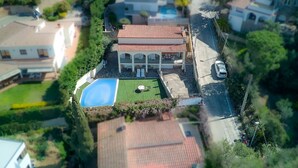 Vista aérea de uma área residencial com uma casa, piscina, alpendre coberto e um carro estacionado por perto.