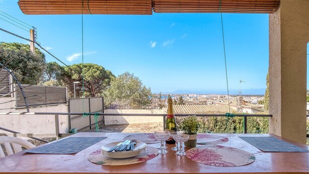 Mesa posta com pratos, talheres e taças de vinho, com vista para a paisagem urbana.