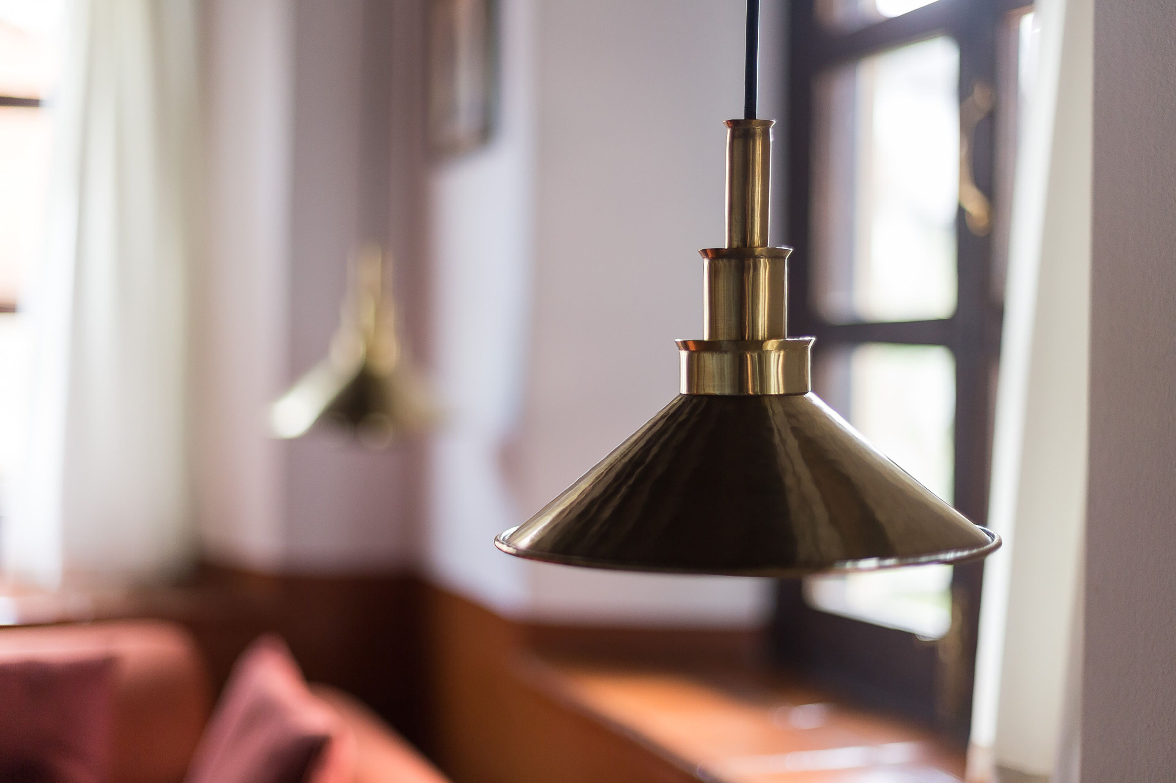 Een hanglamp in een ruimte met een houten bank en een raam.