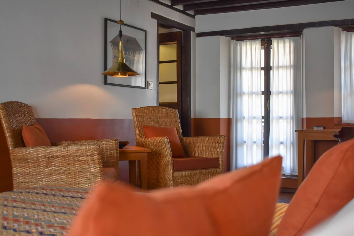 Une pièce meublée de mobilier en osier, avec un lit recouvert d’une couvre-lit à motifs, une table et une lampe suspendue.