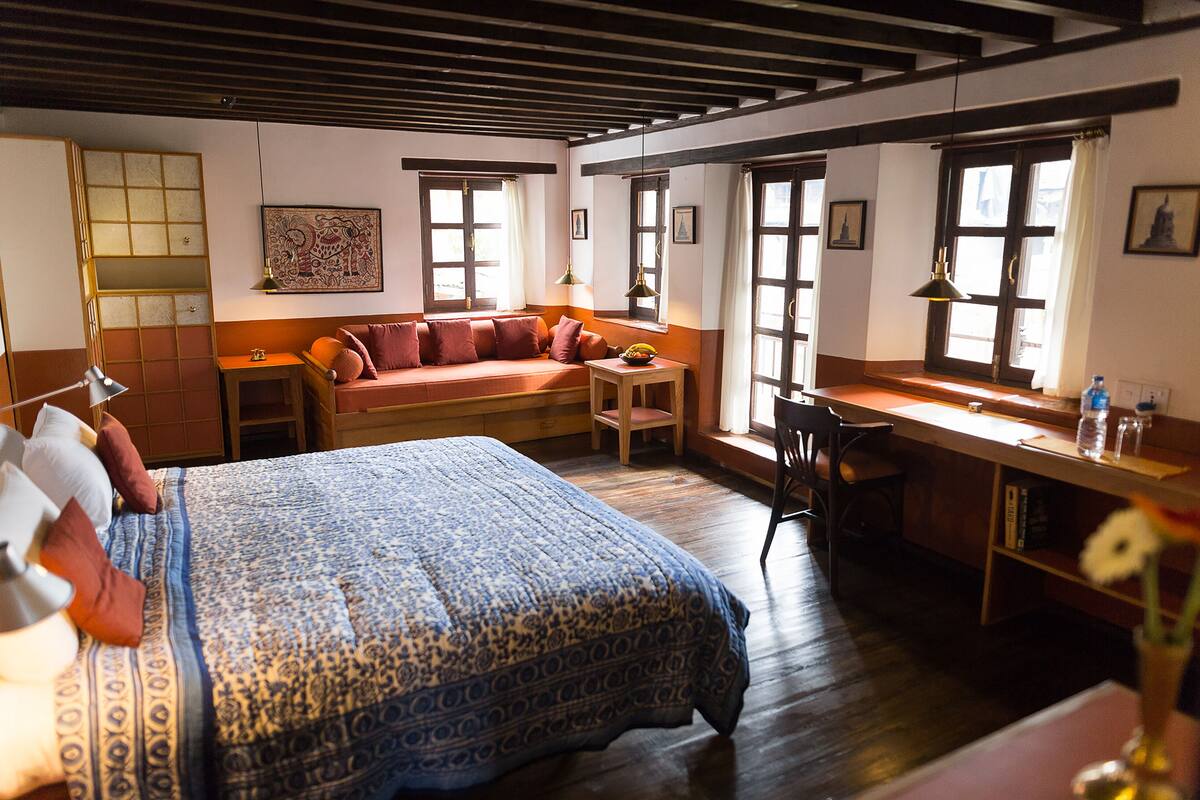 Une pièce comprenant un grand lit, un canapé, un bureau et une chaise. On y trouve également des fenêtres, une lampe et un tableau au mur.